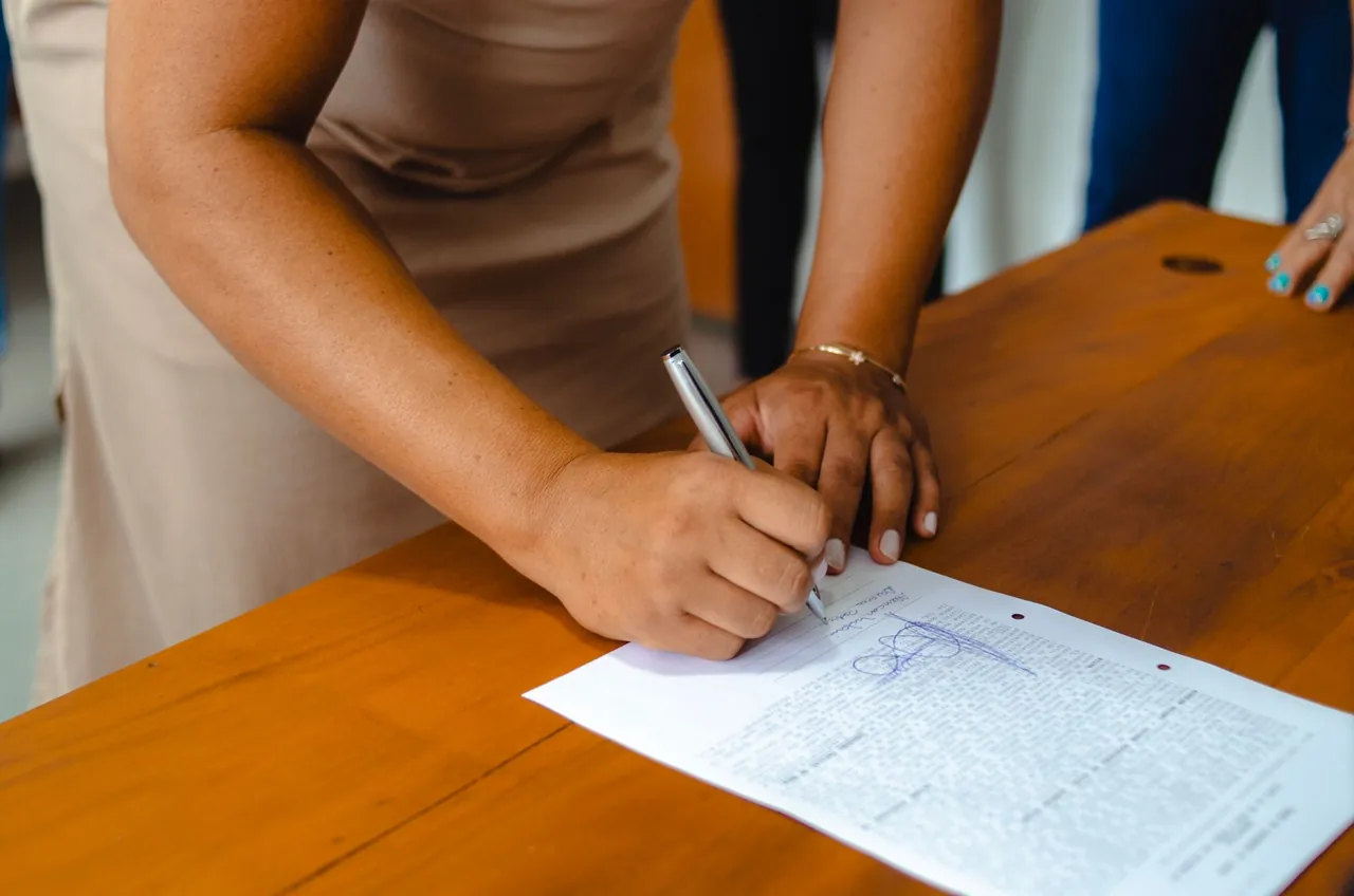 A woman signing an official document on a wooden table